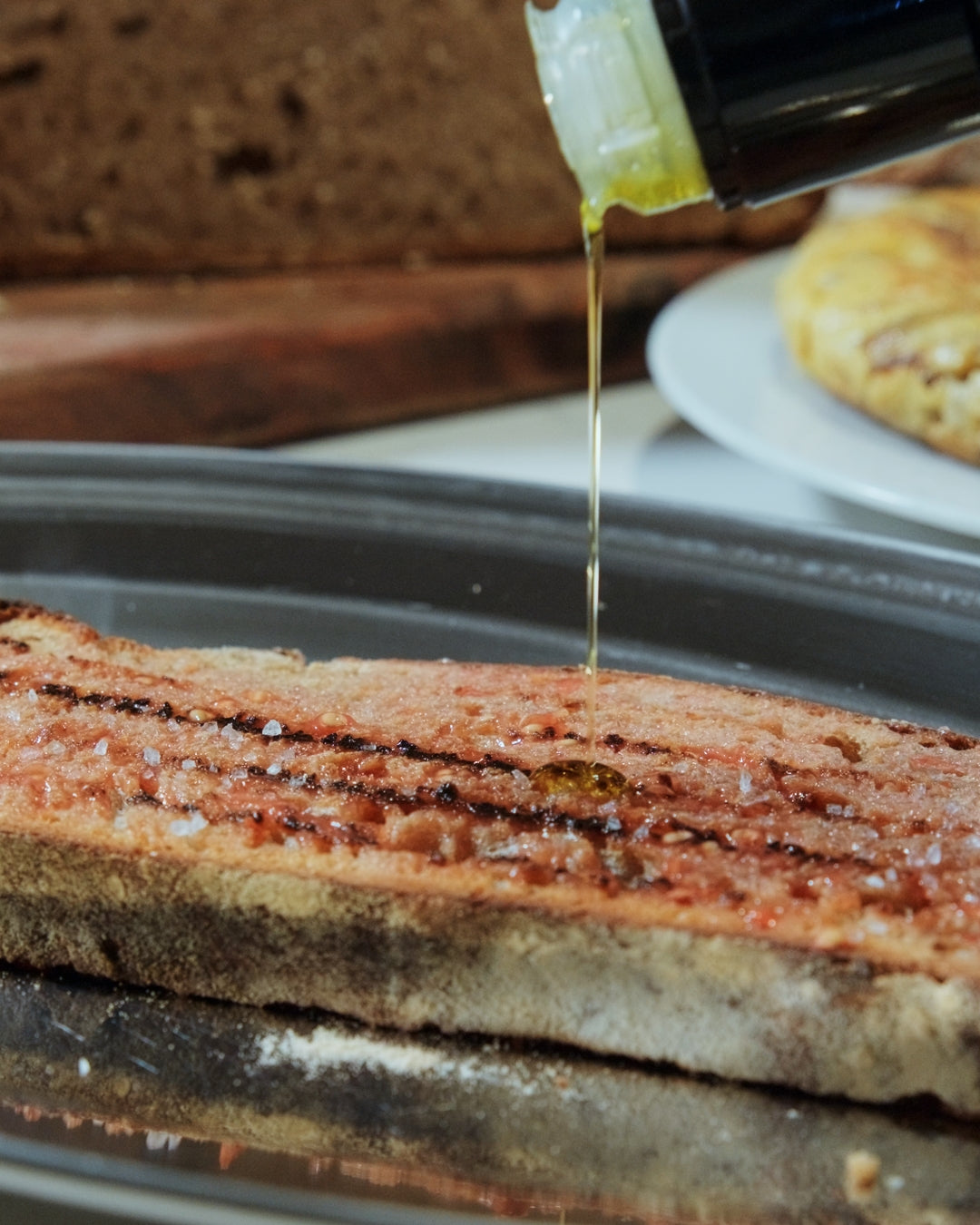 Extra virgin olive oil being drizzled onto a piece of bread with a blurred background